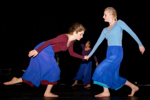 Two dancers interact in a choreographed piece, with a third dancer in the background.