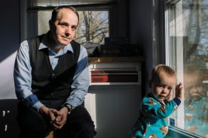 Leeman Kessler '04 and toddler son Martin sit in a dining room. Leeman looks at the camera while Martin, in pyjamas, looks out the window.
